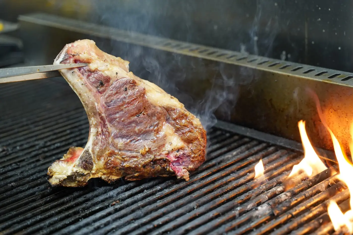 Una bistecca alla fiorentina sulla griglia, con la fiamma accanto