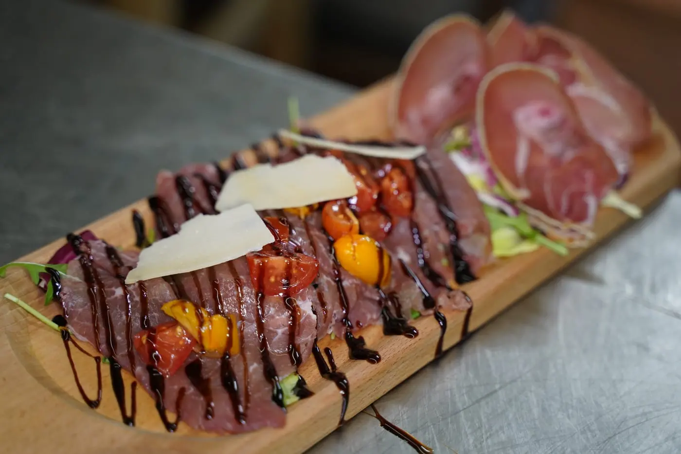Un tagliere di carpaccio con scaglie di formaggio, pomodorini e prosciutto