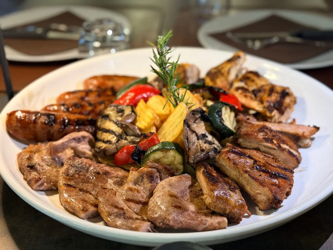 Un piatto di grigliata mista con salsicce, pollo, costine e verdure