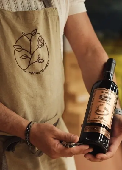 Una bottiglia di rosso toscano nelle mani di chi la serve, col grembiule ricamato del logo di Fantastic Garden