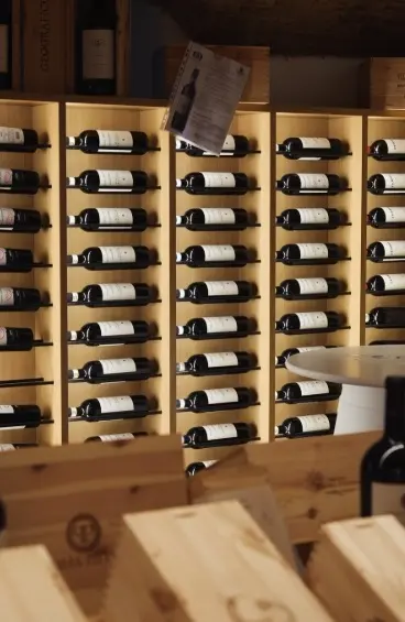 Le rastrelliere a muro della cantina, piene di bottiglie coricate, con le casse di legno in primo piano