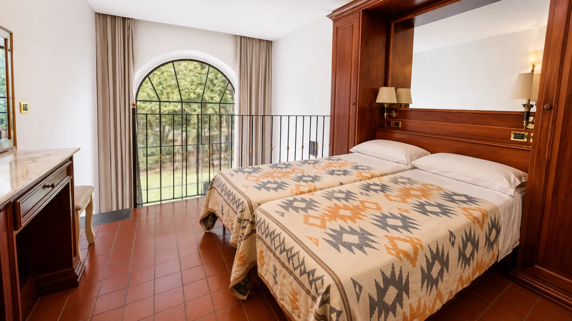 Un loft con i due letti singoli, la testiera in legno e la portafinestra ad arco con il balconcino sul giardino