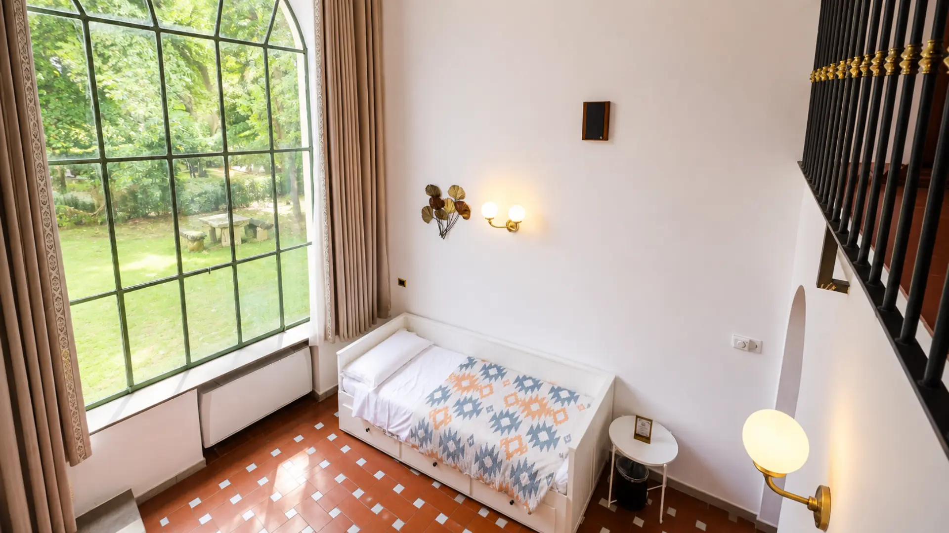 Il divano letto di un loft sotto la vetrata alta che dà sul parco, con la ringhiera del soppalco a destra