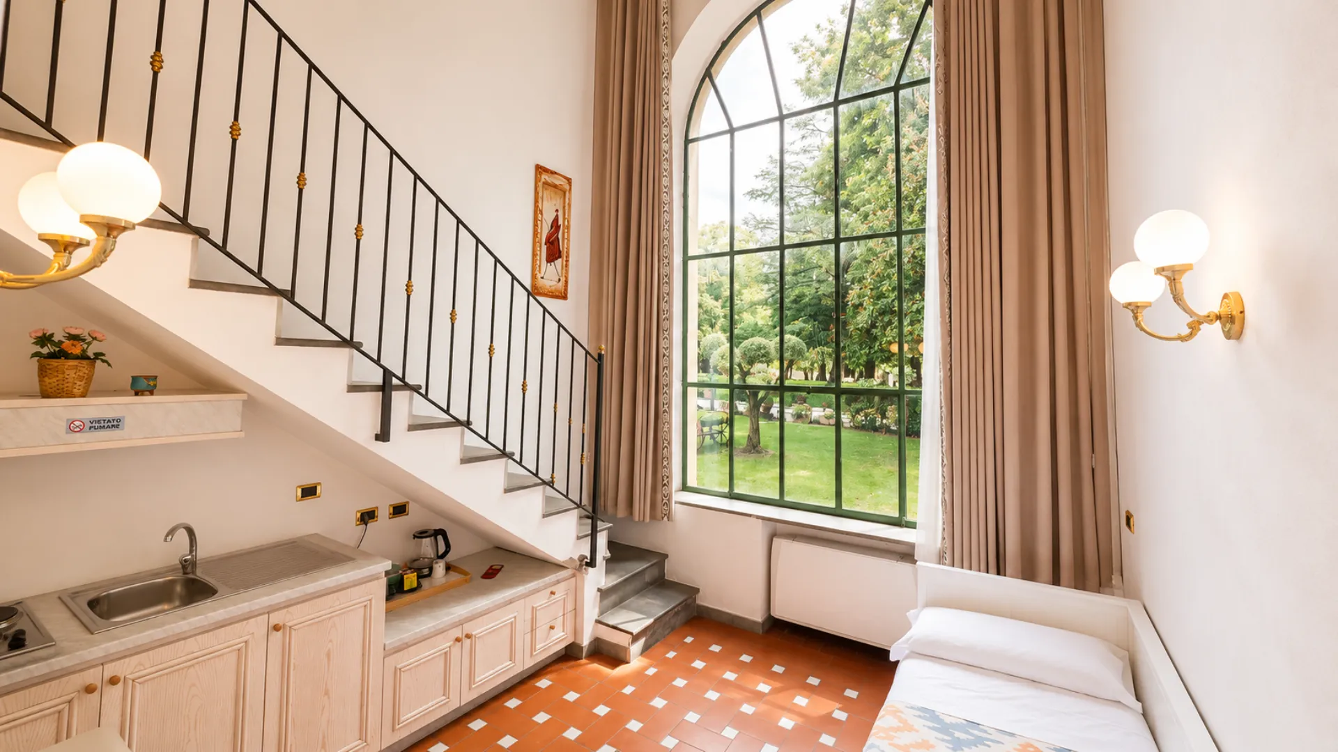L'ingresso di un loft su due piani: la scala che sale al soppalco, l'angolo cottura e la vetrata alta sul parco