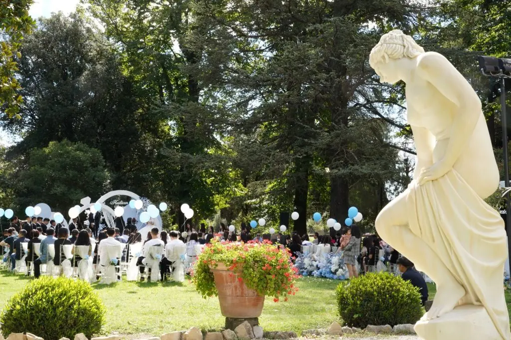 Una cerimonia nel parco della villa, con gli ospiti seduti fra gli alberi e i palloncini bianchi e azzurri