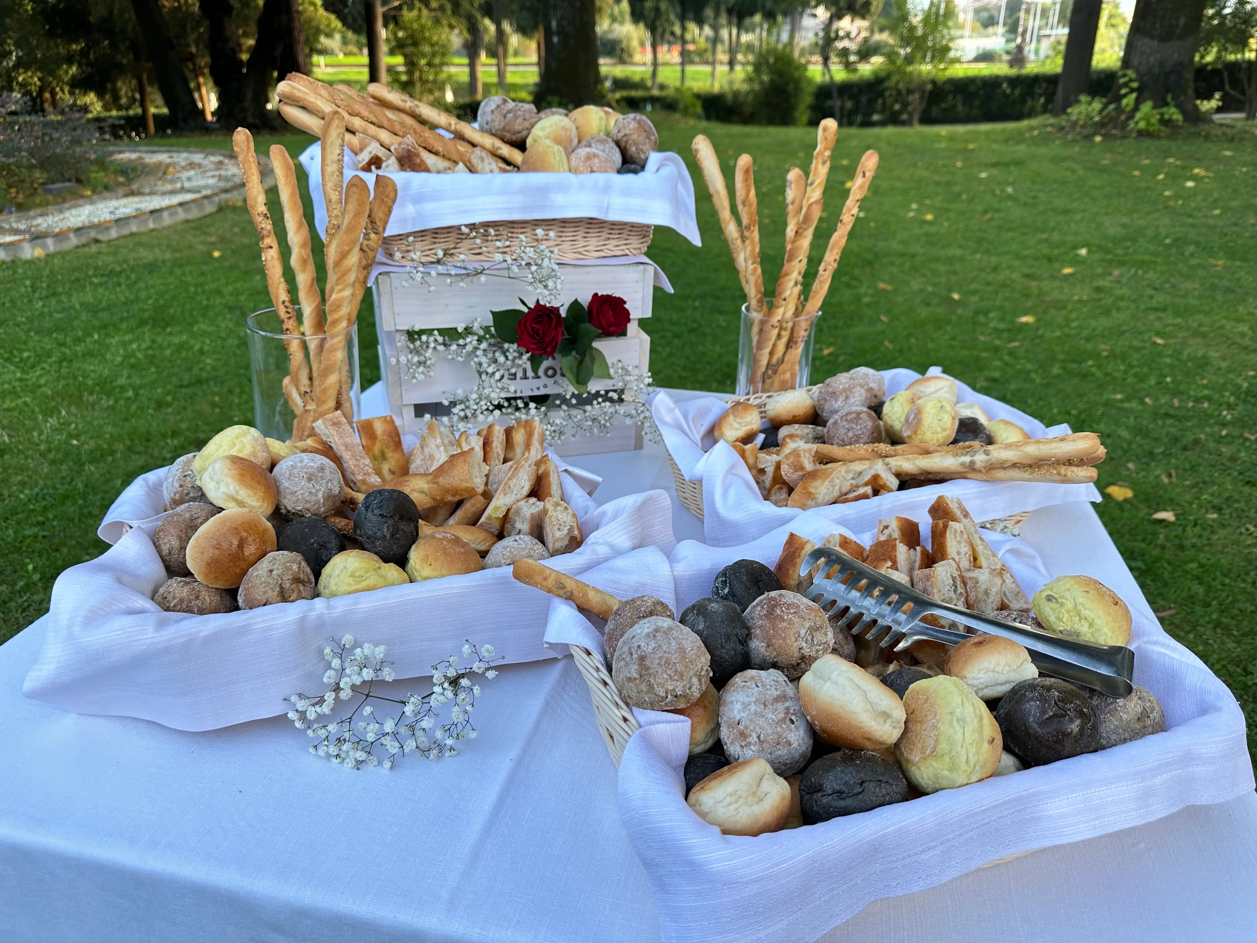 Il buffet del brunch apparecchiato nel parco: cestini di pane, grissini e brioche su una tovaglia bianca