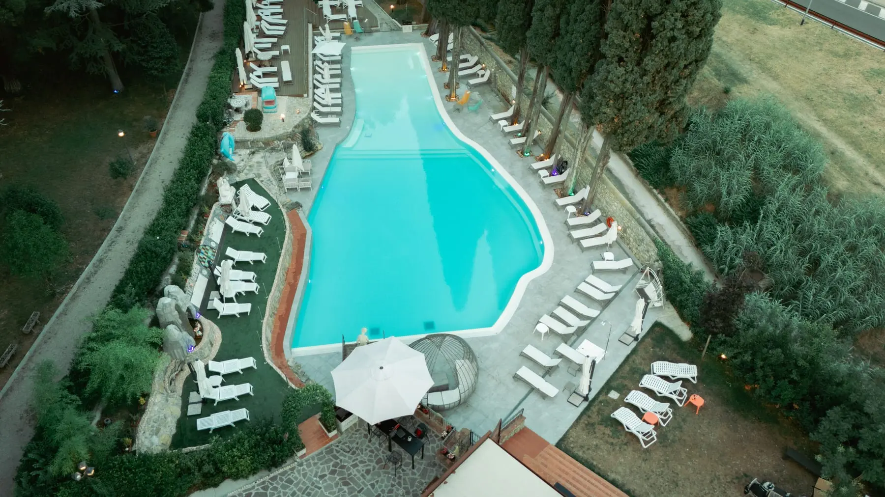 La piscina vista dall'alto al tramonto, con i lettini tutt'intorno e le luci accese