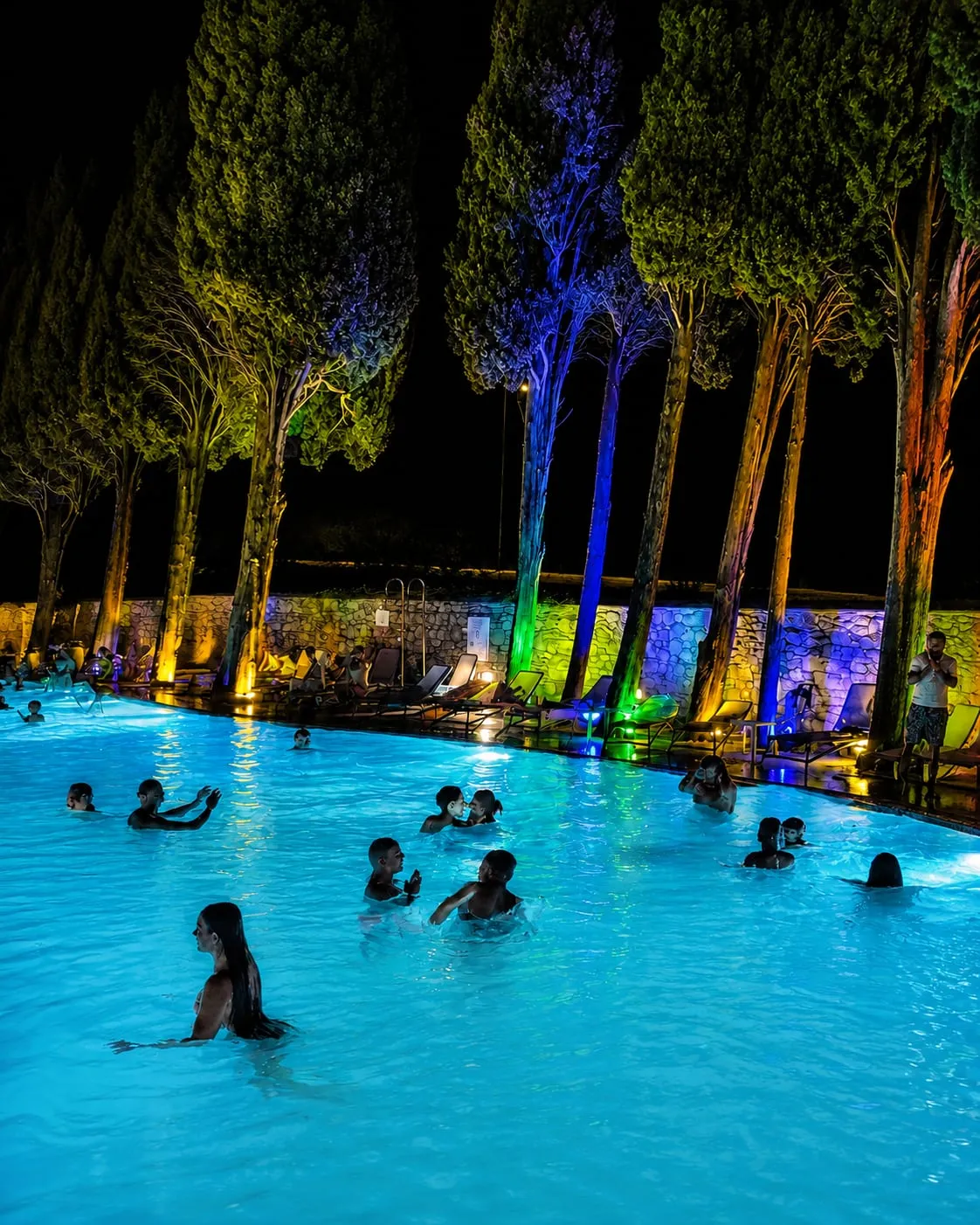 La piscina di notte, con i cipressi illuminati di blu, verde e arancio