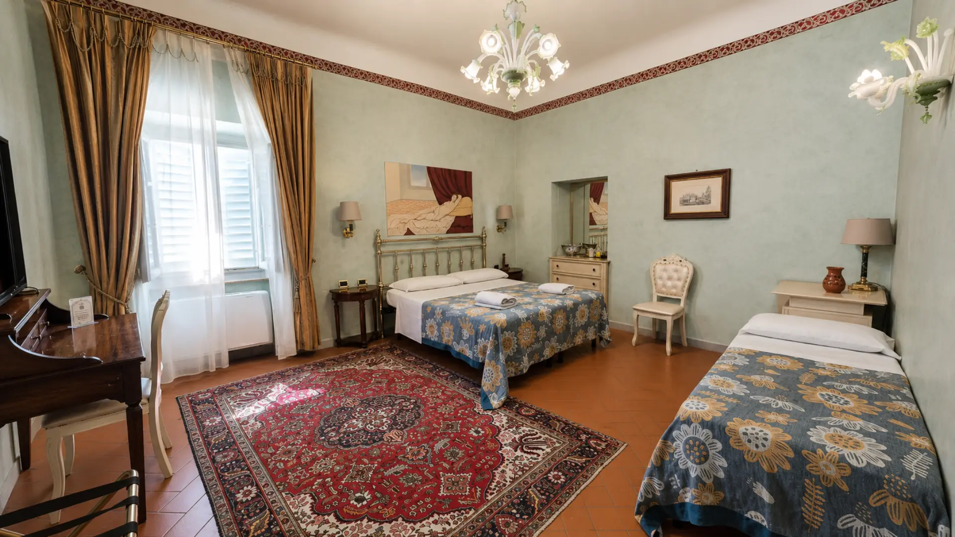 Una camera Premium con le pareti verde salvia, il letto in ottone e il lampadario di vetro soffiato