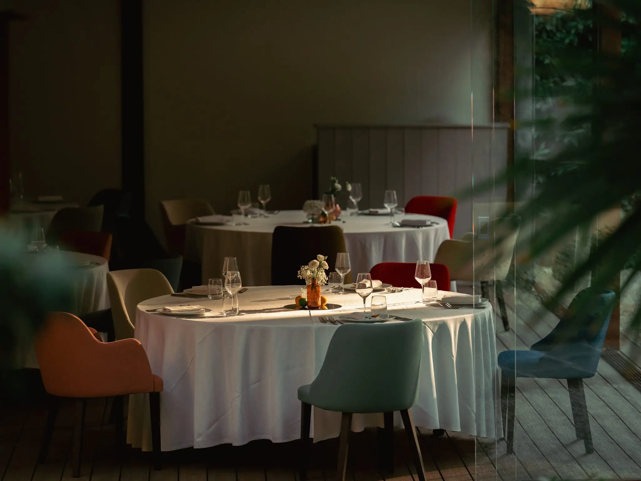 Il salone del ristorante nella Limonaia, con i tavoli rotondi apparecchiati, le sedie in velluto colorato e le vetrate sul parco